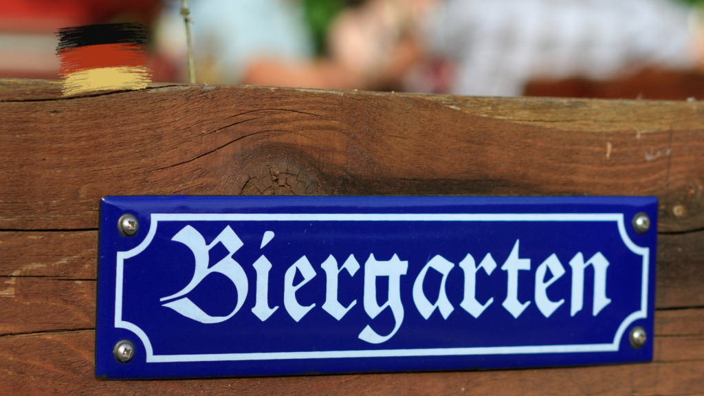 青いプレートに白い筆記体で「Biergarten」と書かれた看板が木製の表面に取り付けられている。